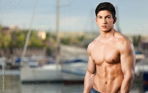 Sexy portrait of muscular handsome topless male model at the beach background.