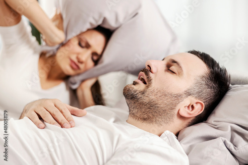 A man snoring and sleeping in the bed while woman is annoyed of it.
