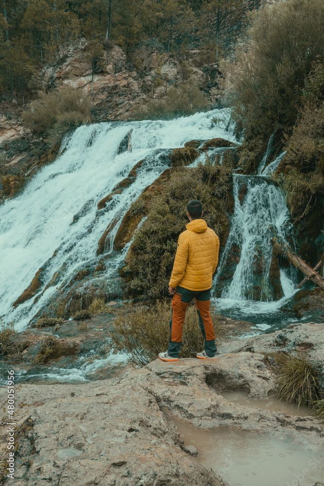 Boy in yellow jacket looking at a waterfall in the middle of a forest