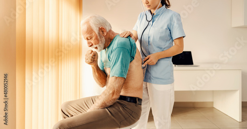 A sick old man coughing and getting medical attention by a female doctor in doctor's office. Heath care, medical support and medical service. photo