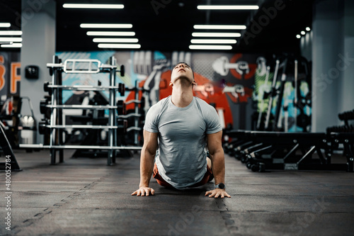 A muscular sportsman doing yoga exercise in cobra pose in a gym.