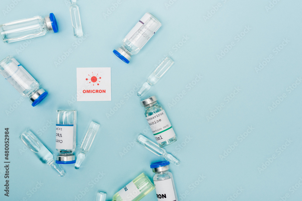 top view of vaccine vials and ampoules near card with omicron lettering and bacteria on blue. top view of vaccine vials and ampoules near card with omicron lettering and bacteria on blue.