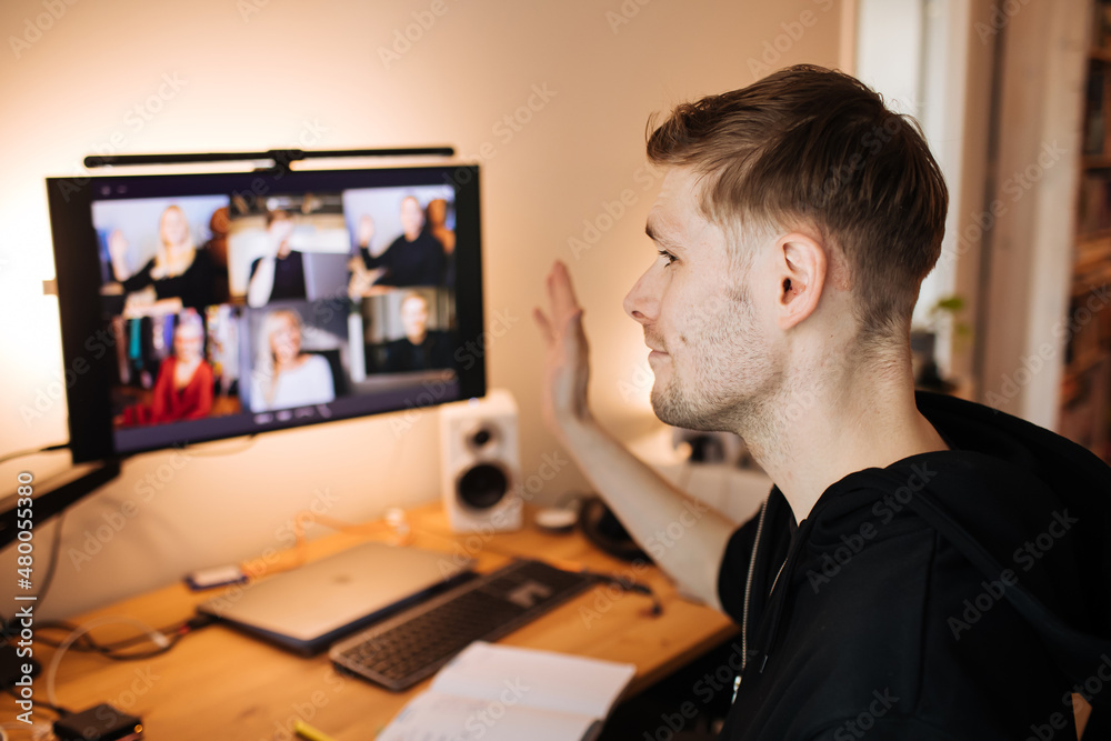 Young man having video conferencing call via computer. Working remotely managing team virtual call Stay at home and work from home. Virtual House party Home office computer desk.	
