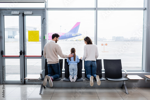 parents looking at daughter near window in airport.