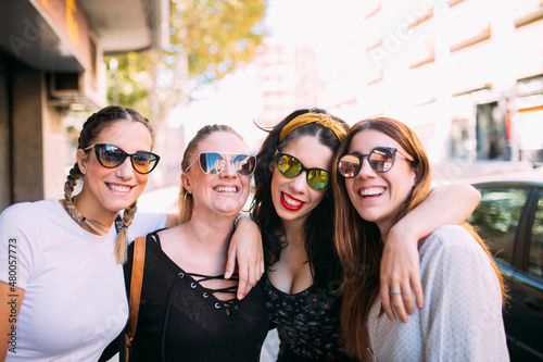 Group of 4 young women friends enjoying a sunny day in the city, posing for a picture looking straight ahead