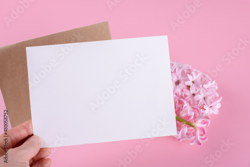Hand holding blank wedding invitation stationery card mockup with envelope on pink background with hyacinth flowers, feminine blog. Valentines day card, valentines day background, mothers day