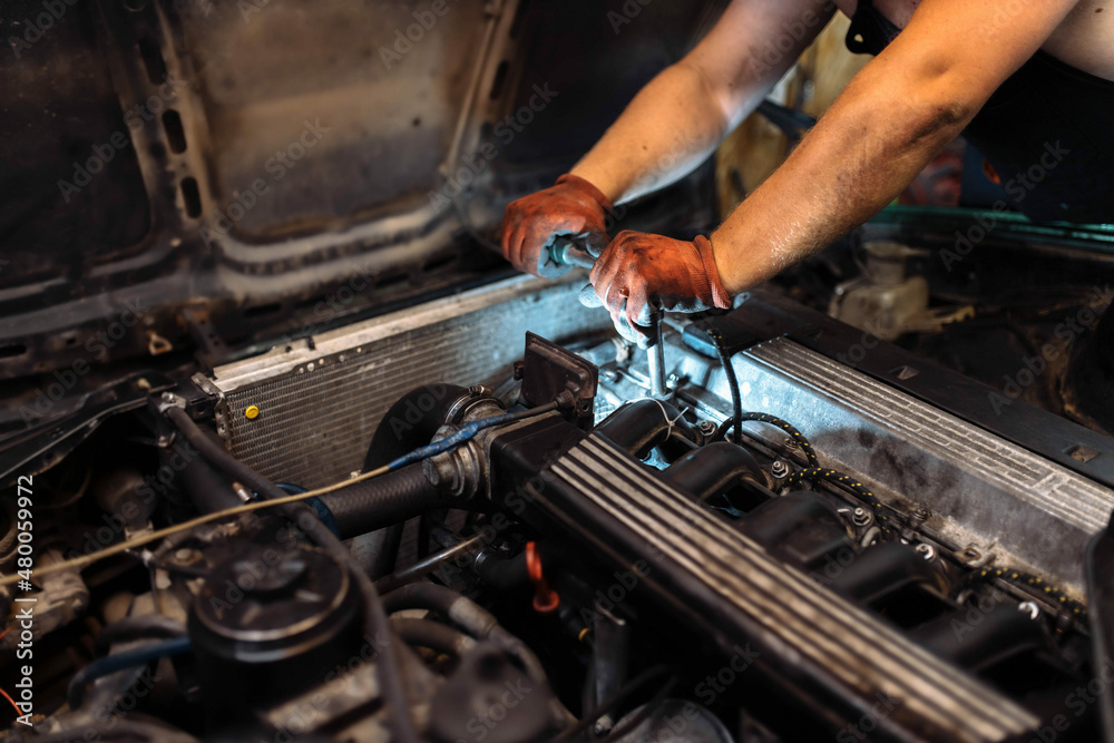 repairing a car engine in a car service, the hands of a mechanic unscrew the bolts repairing a car engine in a car service, the hands of a mechanic unscrew the bolts