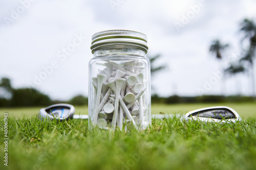 many golf tees in a jar with two clubs close up