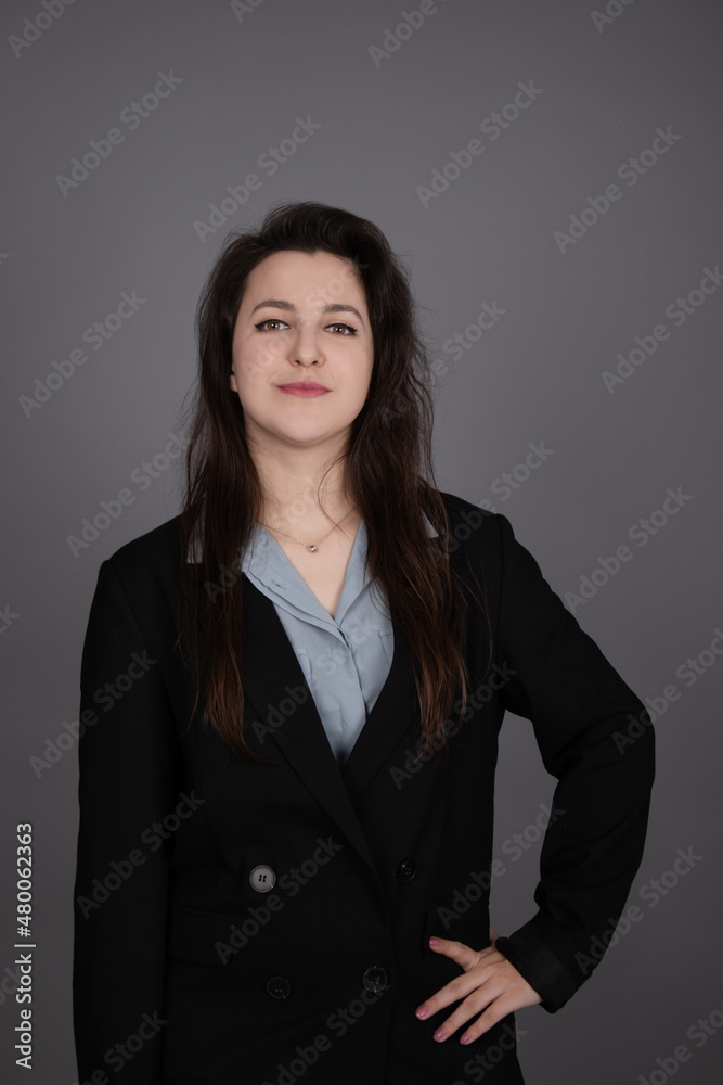 attractive confident brunette business woman in blue blouse and black jacket on grey background. attractive confident brunette business woman in blue blouse and black jacket on grey background.