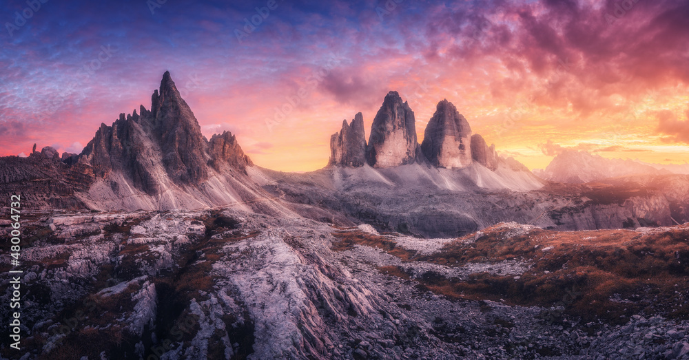 Mountains and beautiful sky with colorful clouds at sunset. Summer landscape with mountain peaks, stones, grass, trails, violet sky with red clouds. High rocks. Tre Cime in Dolomites, Italy. Nature