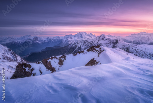 Snow covered mountains and colorful purple sky with clouds at sunset in winter. Beautiful wintry landscape with snowy rocks and hills at dusk. Scenery with alps at frosty evening. Alpine mountains © den-belitsky