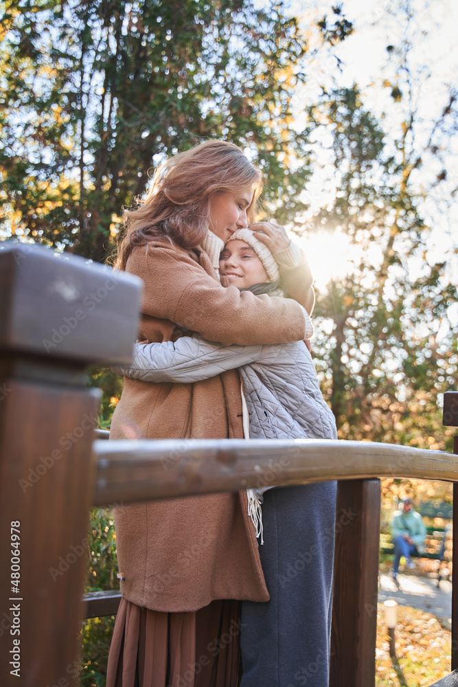 Naklejka premium Lovely woman and her teen daughter embracing at the urban park outdoors