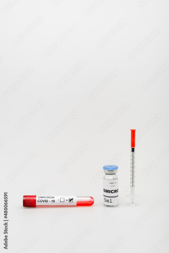 test tube with positive result near covid-19 omicron variant vaccine and syringe on grey background. test tube with positive result near covid-19 omicron variant vaccine and syringe on grey background.