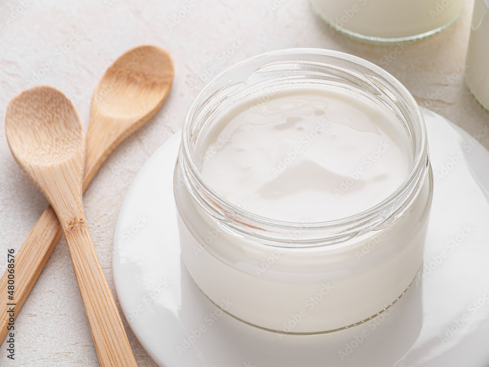 Glass jar of homemade yogurt with wooden spoons on white table. Horizontal. Close up.