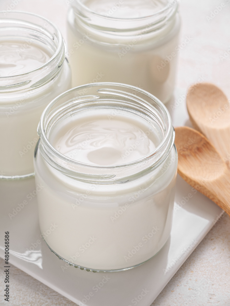 Glass jars of homemade plain yogurt with wooden spoons on white tray. Vertical. Close up. Glass jars of homemade plain yogurt with wooden spoons on white tray. Vertical. Close up.