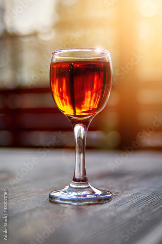 Glass of cognac on wooden table in the sunlight. Shot glass.