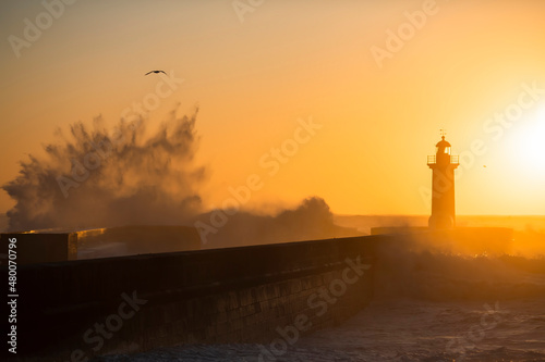 Huge wave on the lighthouse in the background on the golden sunset. Atlantic ocean, Porto, Portugal.