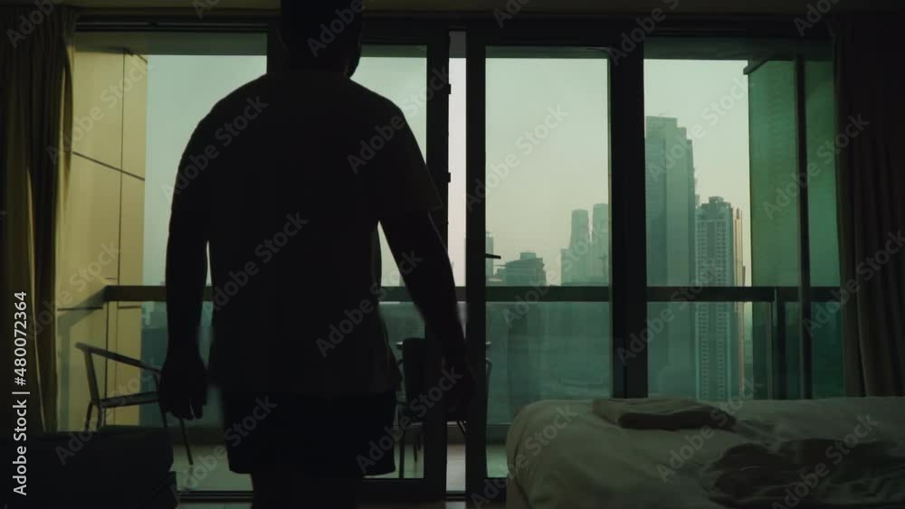 A guy in a white T-shirt with a panoramic window overlooking the skyscrapers and opens it with his hands. Megapolis. Apartment on a very high floor in Dubai A guy in a white T-shirt with a panoramic window overlooking the skyscrapers and opens it with his hands. Megapolis. Apartment on a very high floor in Dubai
