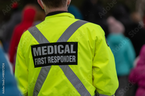 Medical first responders walking along a road wearing black wool stocking caps, yellow reflective coats with the medical first responder in grey letters and across. The EMT is carrying a first aid kit