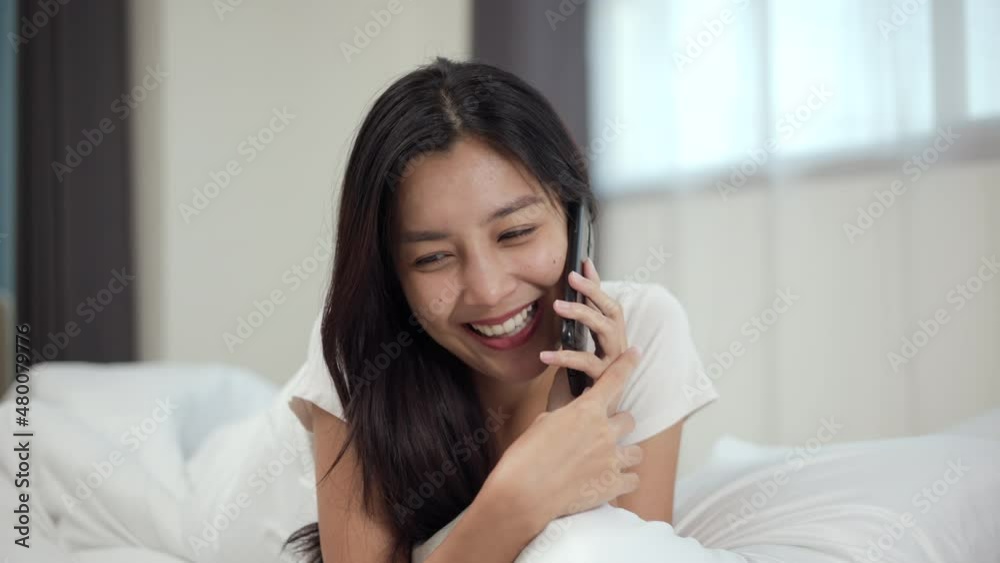 Young beautiful asian woman talking on cell phone, using smart phone on bed to social media at home. Lifestyle of Pretty female using mobile phone to network internet online before sleep. Young beautiful asian woman talking on cell phone, using smart phone on bed to social media at home. Lifestyle of Pretty female using mobile phone to network internet online before sleep.