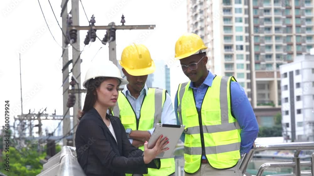 Three engineers wearing hard hats and high-visibility vests review plans on a tablet at a construction site, emphasizing teamwork and project management. Three engineers wearing hard hats and high-visibility vests review plans on a tablet at a construction site, emphasizing teamwork and project management.