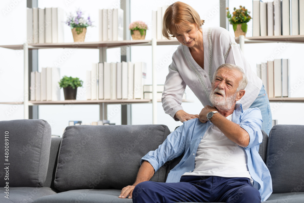 senior woman giving a shoulder massage to her husband on sofa senior woman giving a shoulder massage to her husband on sofa