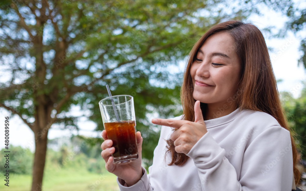 A young asian woman holding and pointing finger at a glass of iced coffee in the outdoors A young asian woman holding and pointing finger at a glass of iced coffee in the outdoors