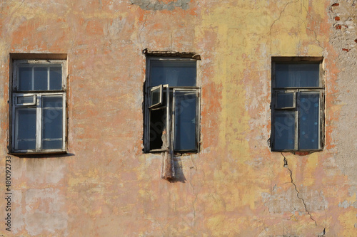 Three rotten windows in the yellow plastered wall of a ruined old brick house