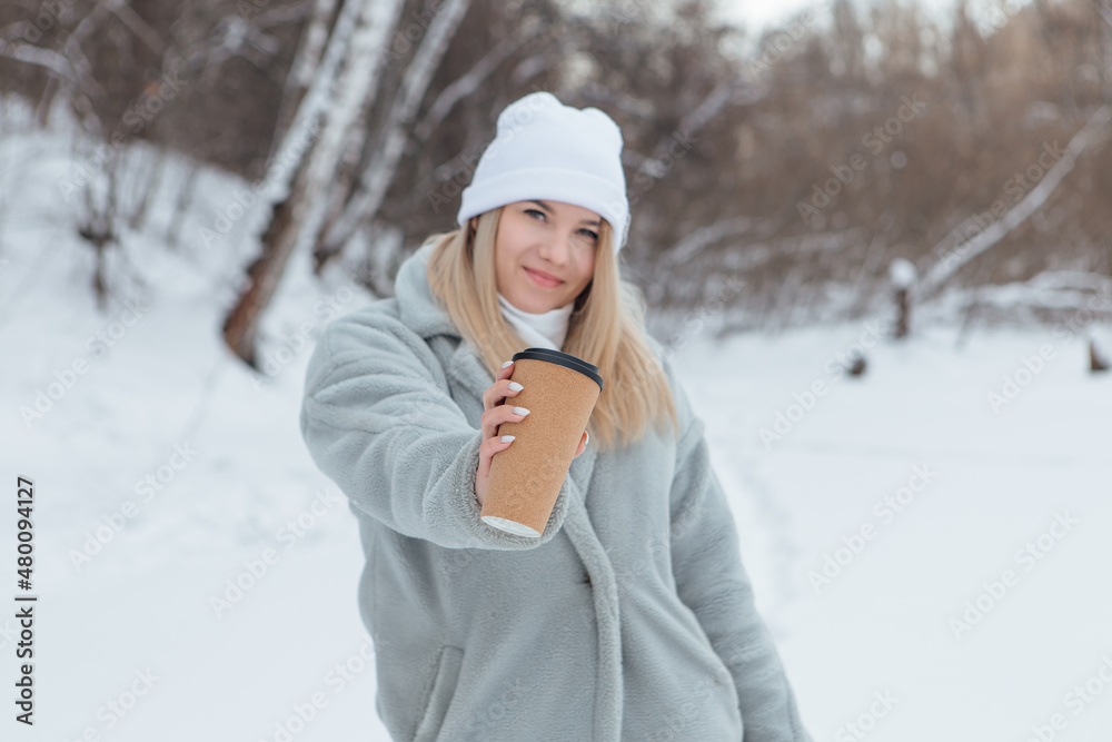 A beautiful young girl smiling and enjoying drinking coffee in a winter forest. A beautiful young girl smiling and enjoying drinking coffee in a winter forest.