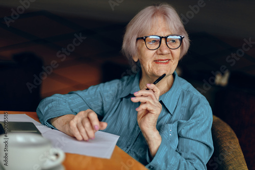 elderly woman with glasses sits at a table in front of a laptop unaltered