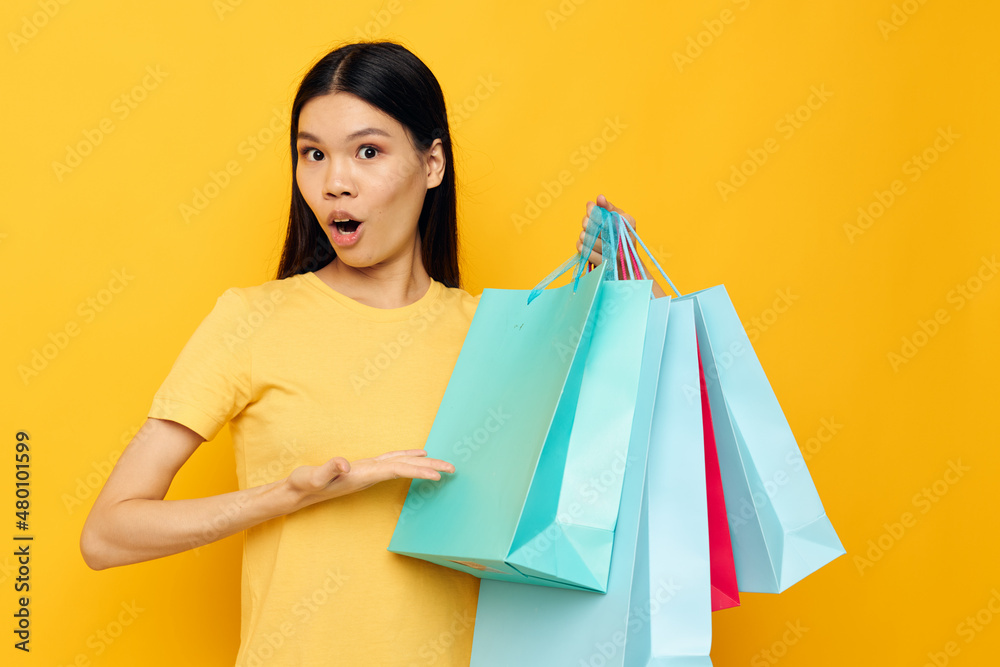 Charming young Asian woman in a yellow T-shirt with multicolored shopping bags studio model unaltered