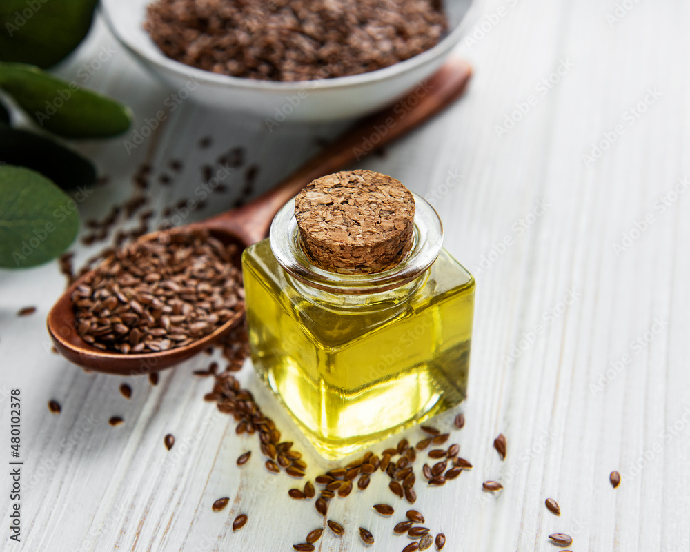 Flax seeds or linseeds in spoon and bowl with glass of linseed oil Flax seeds or linseeds in spoon and bowl with glass of linseed oil