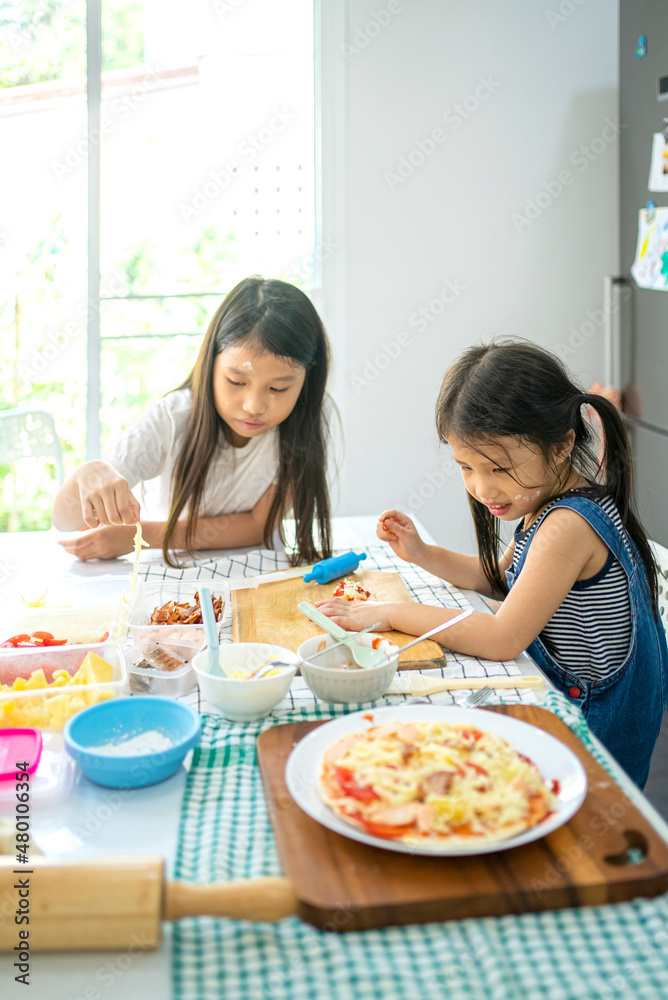 Asian girl in casual dress having fun while make pizza with prosciutto, tomato, cheese, vegetables in home kitchen. family and relationship concept