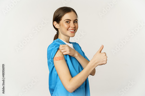 Leinwand Poster Smiling nurse, doctor in scrubs, medical worker showing her vaccinated shoulder