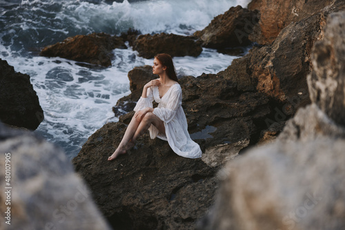 pretty woman with wet hair in white dress sits on waves stones unaltered