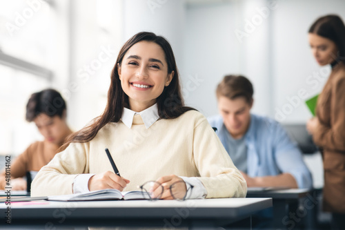 Smiling female student sitting at desk writing in her notebook photo