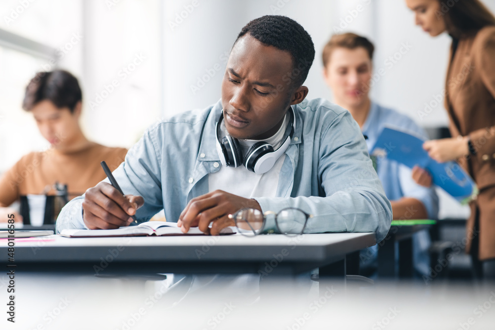Black male student sitting at desk in classroom writing exam Black male student sitting at desk in classroom writing exam