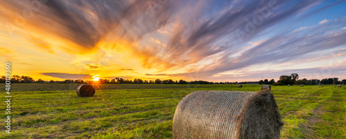 Slika na platnu Beautiful sunset over green meadow with hay bales
