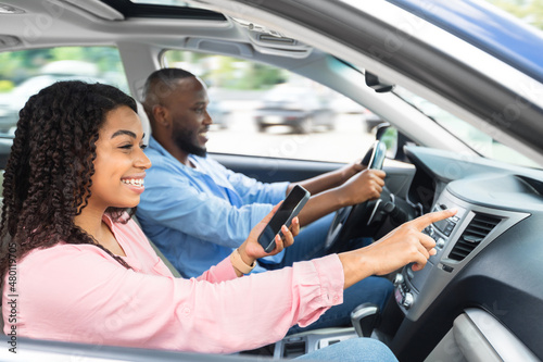 Happy black couple driving car and using cell phone