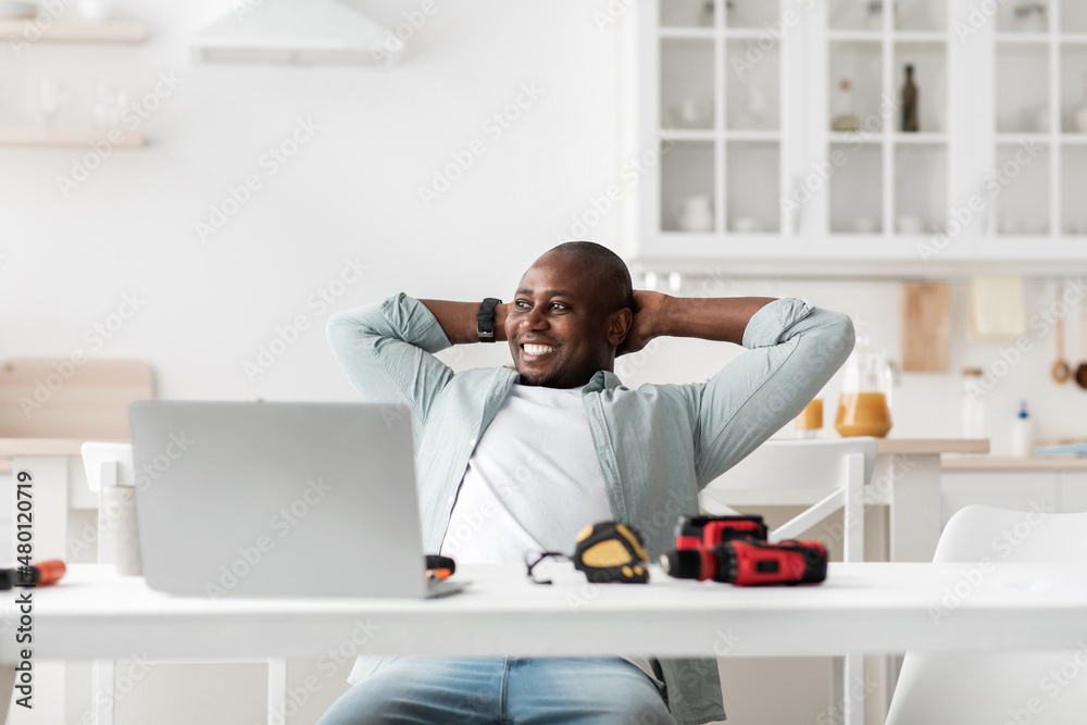 Handyman blogger. Excited african american man resting with hands behind head after working on laptop computer