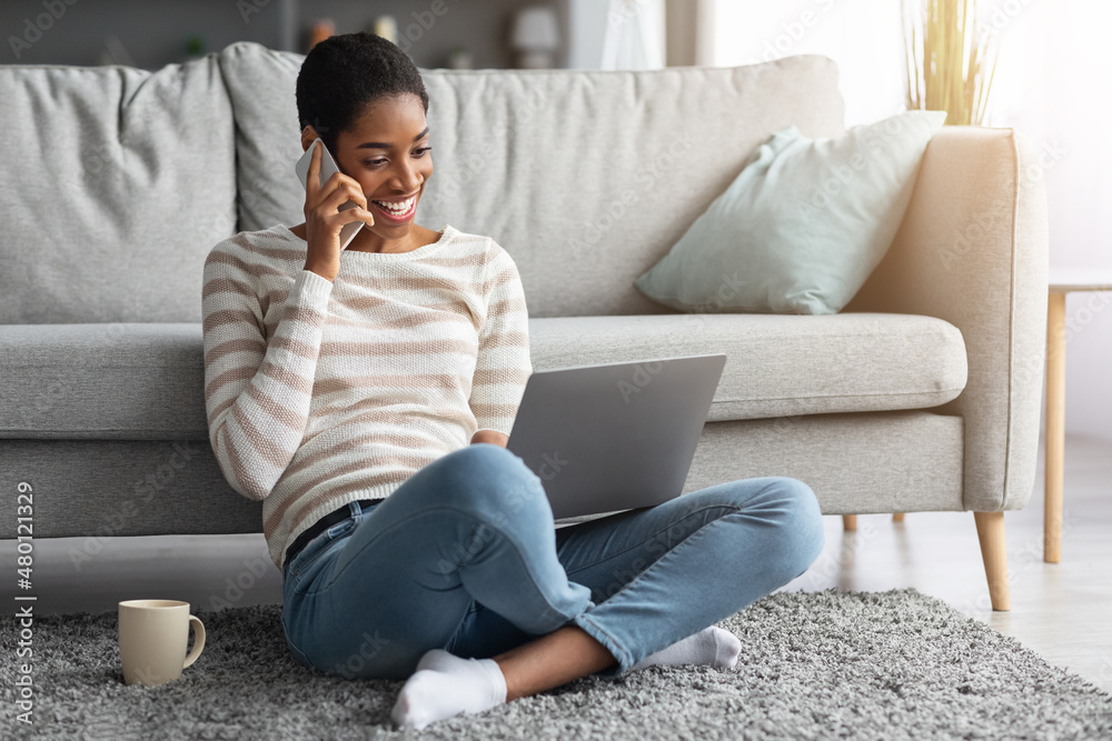 Joyful African American Woman Talking On Cellphone And Using Laptop At Home Joyful African American Woman Talking On Cellphone And Using Laptop At Home