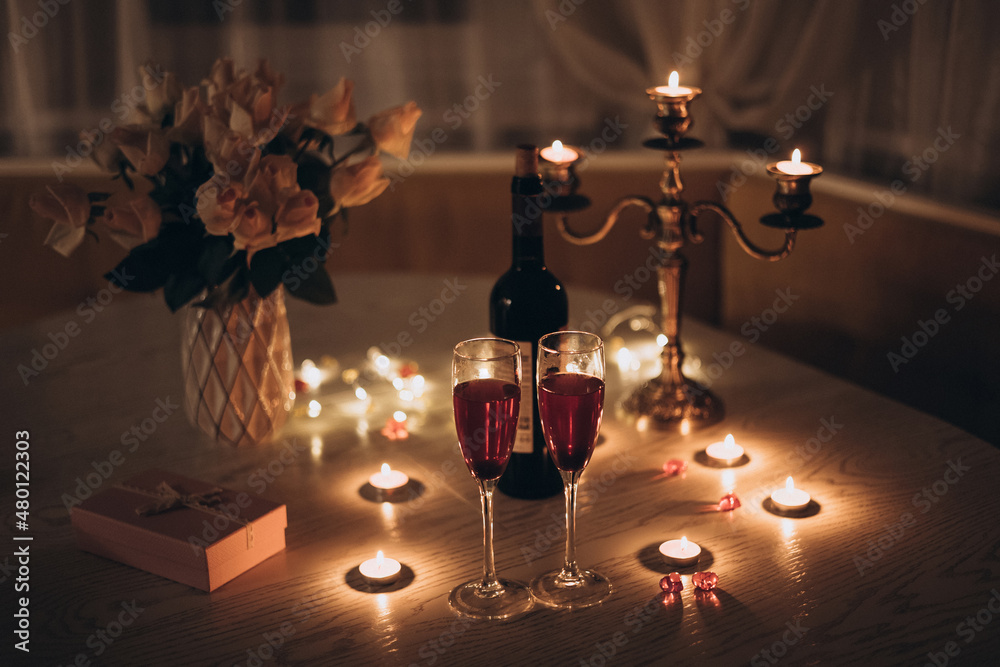 Candlelight date. Glasses with wine candles bouquet of rose and gift box on  table. Romantic candlelight dinner at home at night Stock Photo | Adobe  Stock