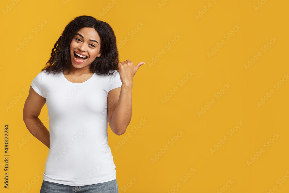 Cheerful black woman pointing aside, showing free space for your design or advertisement, yellow background Cheerful black woman pointing aside, showing free space for your design or advertisement, yellow background