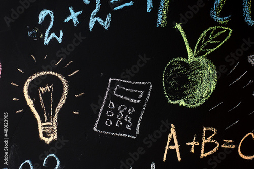 school board with formulas and drawings drawn in chalk. light bulb, apple, calculator