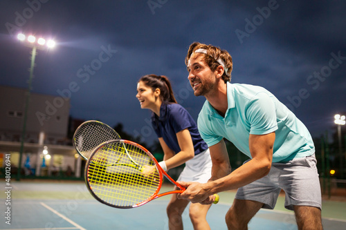 Beautiful young people are playing tennis as a team on tennis court outdoors. People sport concept © NDABCREATIVITY