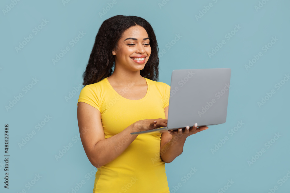 Online education programs. Happy black woman holding and using newest laptop computer over blue background Online education programs. Happy black woman holding and using newest laptop computer over blue background