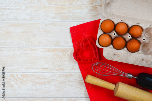 red festive ingrediens for cooking, valentines day eggs in eco package, rolling pin and whisk, cutter dish shape heart for baking cake flat lay