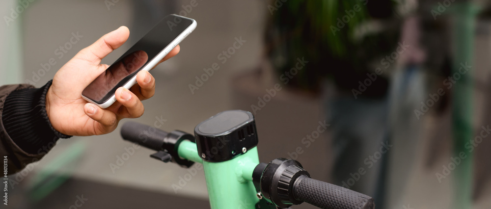 Man using smartphone near public electric scooter on street, banner shot Man using smartphone near public electric scooter on street, banner shot
