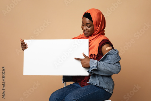 Positive black muslim woman got vaccinated, pointing at blank placard