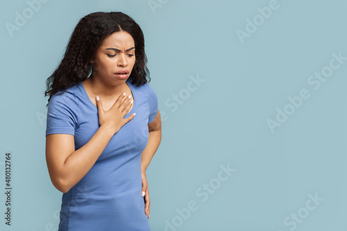 Breathing problem. Sick black woman with chest pain touching inflammated zone over blue background with free space